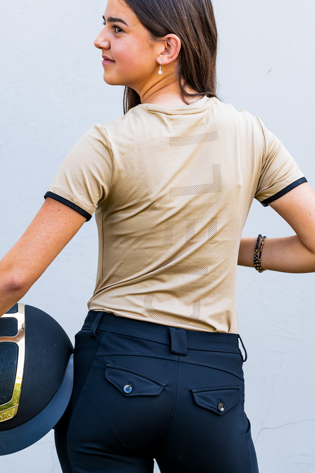 Person wearing a mocha shirt and navy riding pants, holding a helmet against a light blue background
