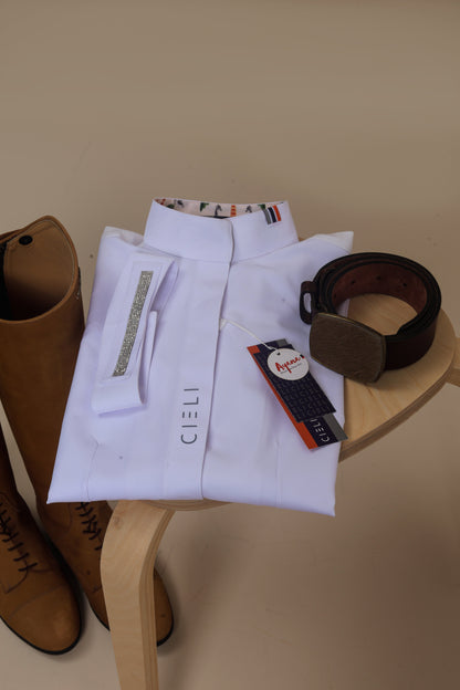 White shirt with a brown belt and riding boots on a wooden stool against a beige background