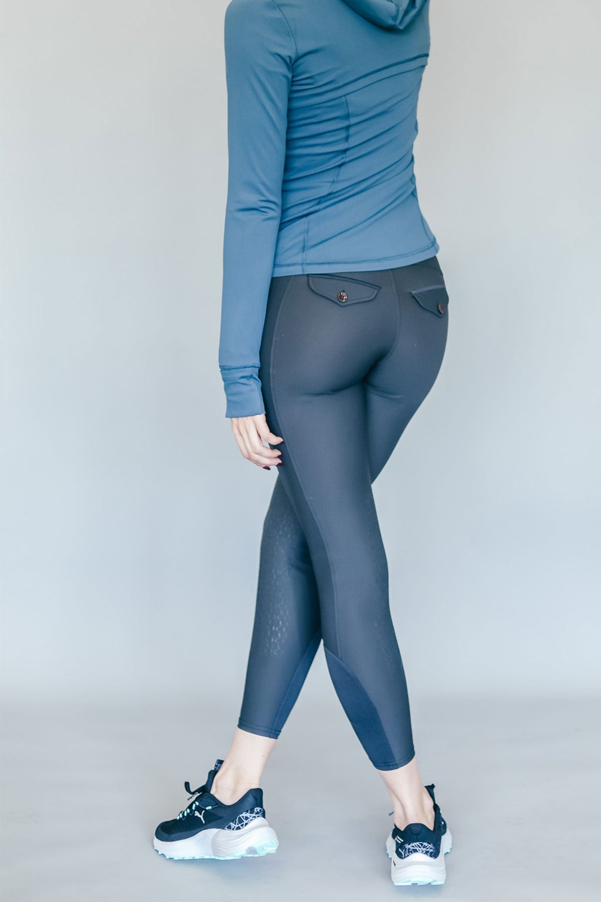 Person wearing a blue hoodie and gray breeches on a plain background