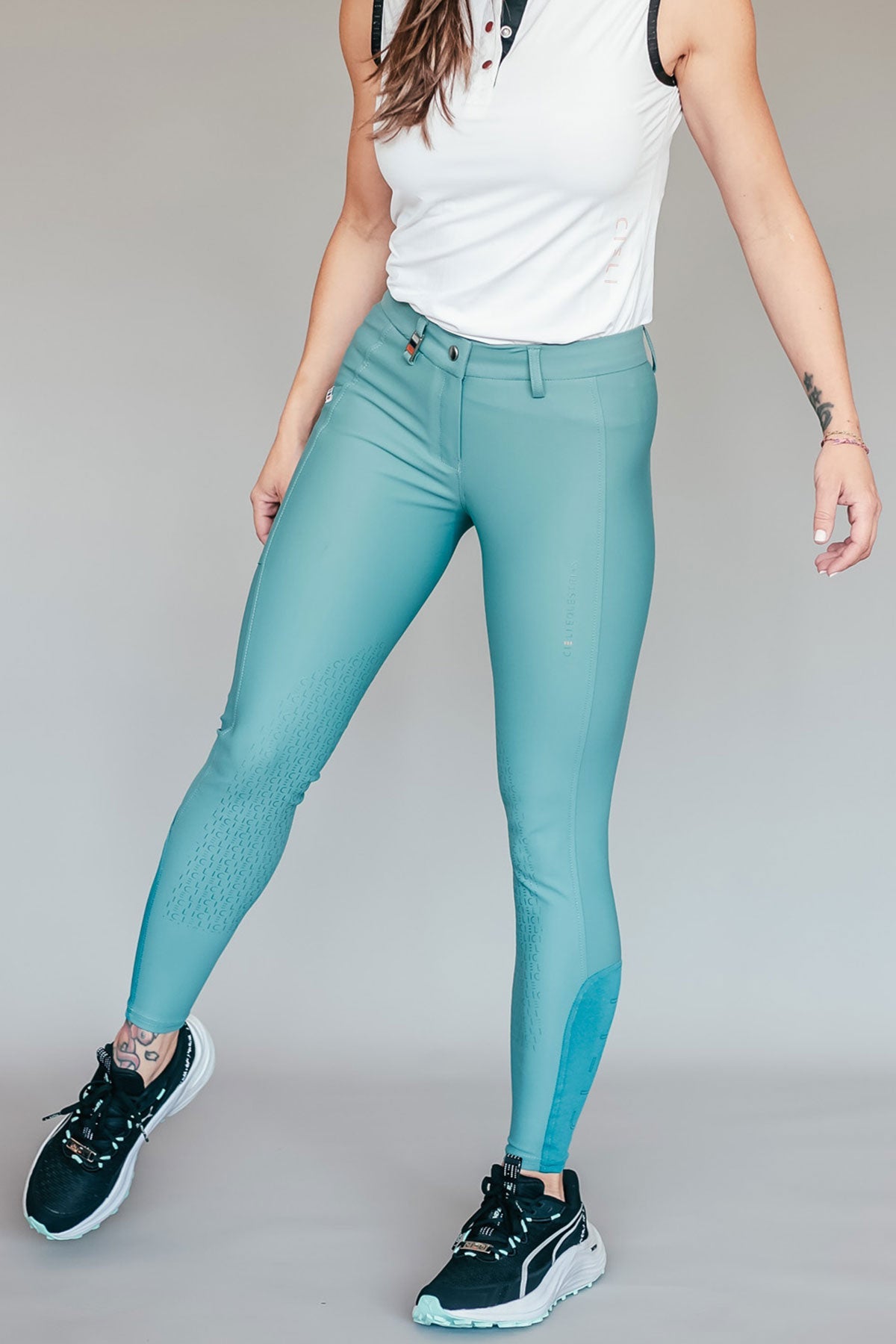 Person wearing teal riding pants on a plain background