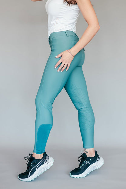 Teal breeches worn by a person on a plain background