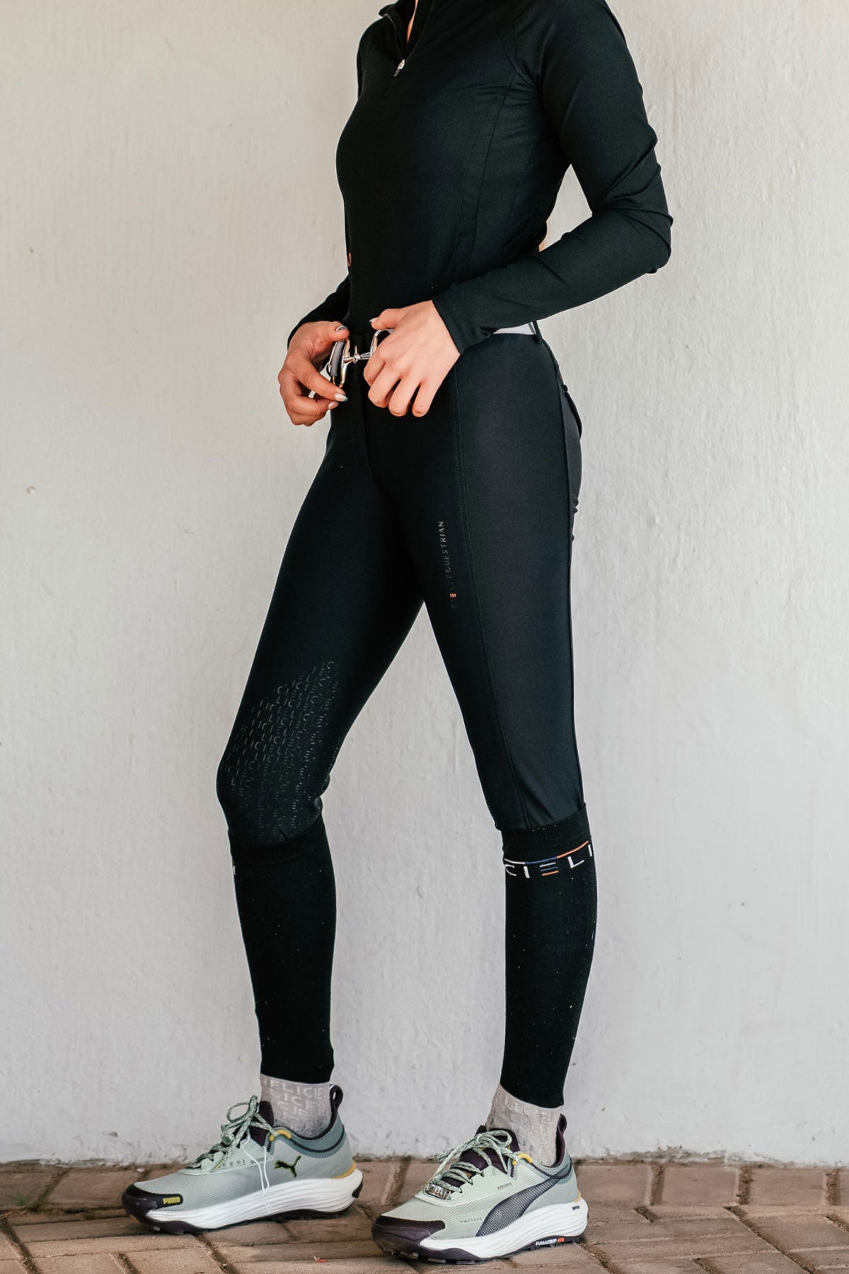 Person wearing black athletic breeches and shoes against a white wall.