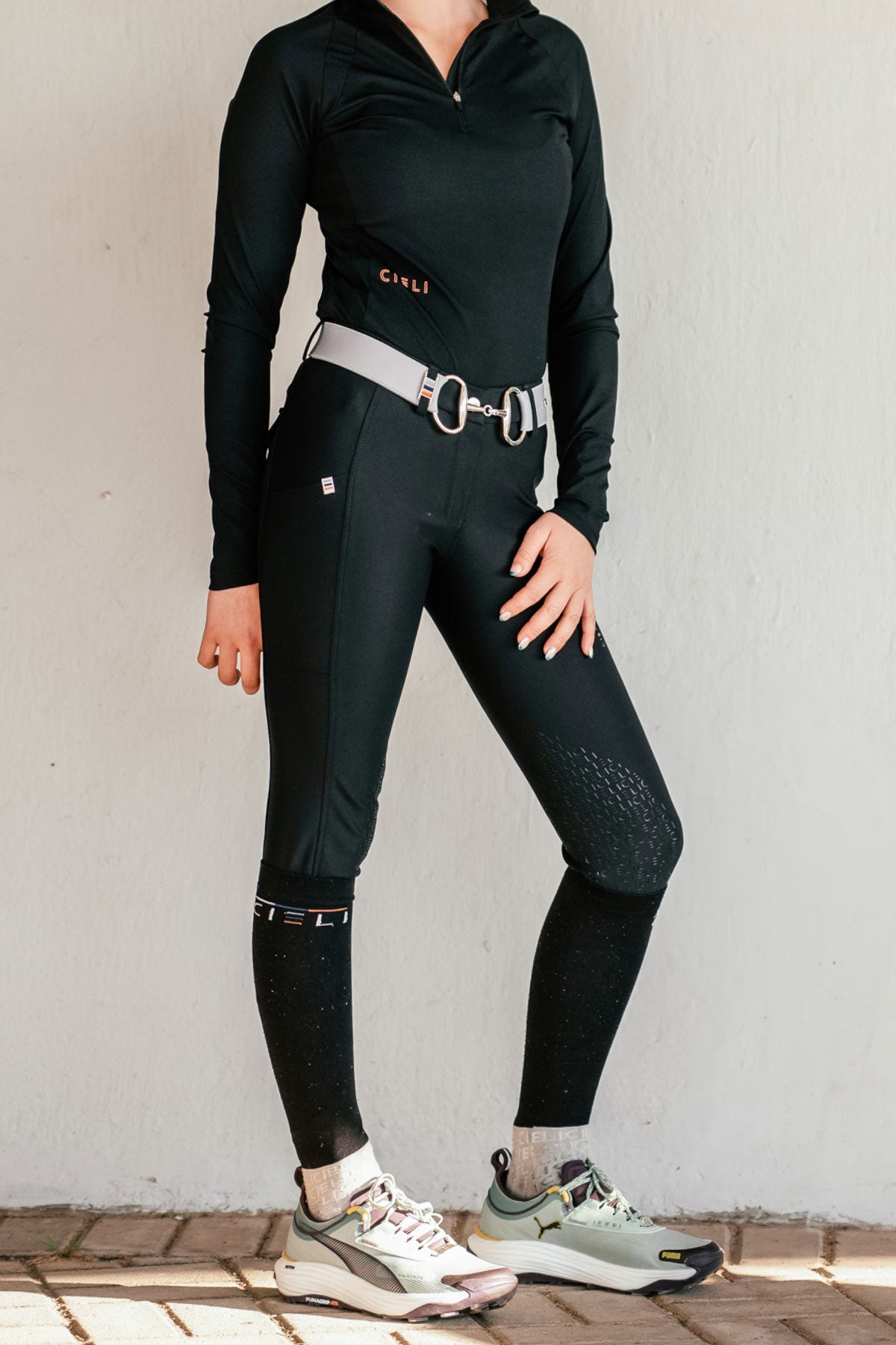 Person wearing a black shirt and breeches with a grey belt on a light background