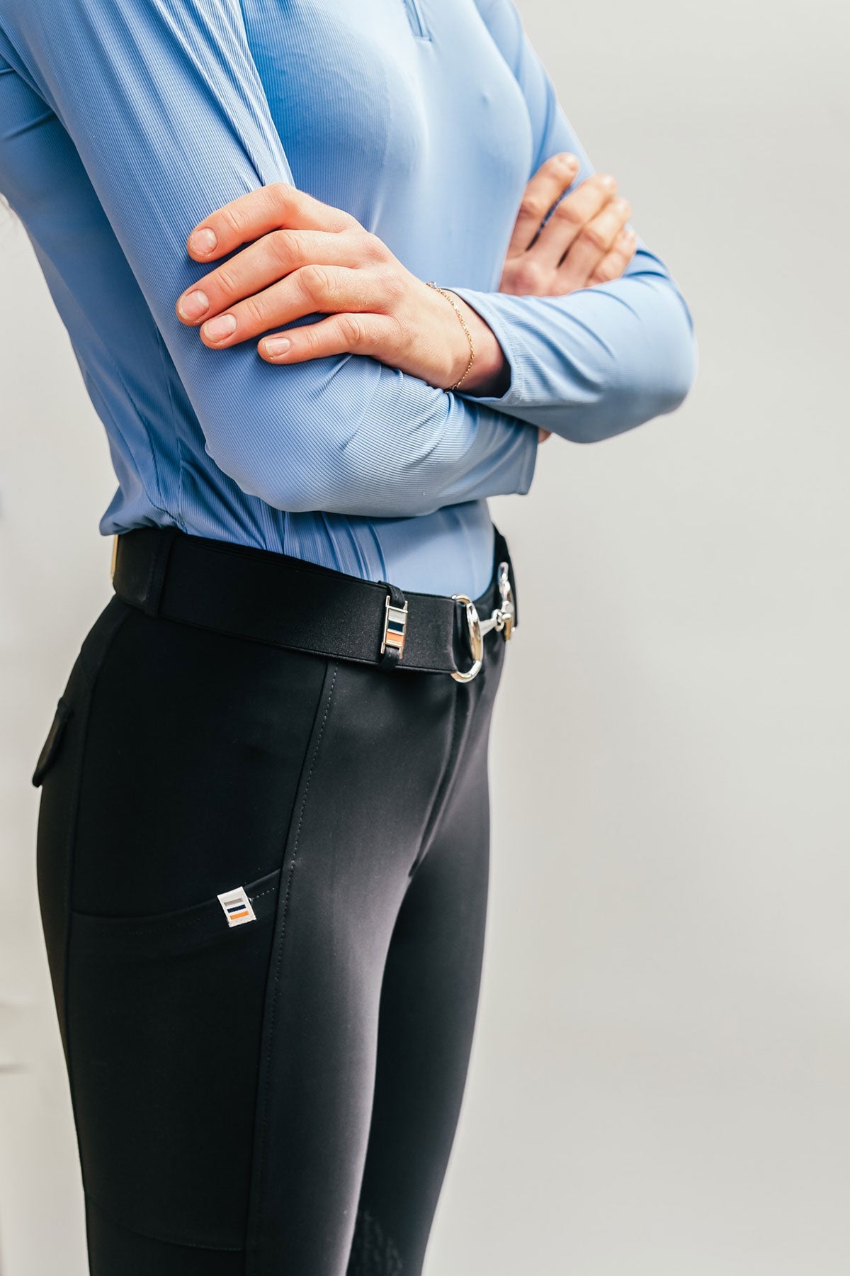 Person wearing a blue top and black riding pants against a plain background