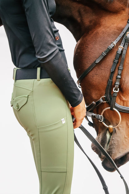 Person wearing green riding pants with a horse in the background