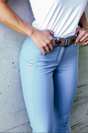Person wearing light blue riding pants with a white top against a concrete wall.