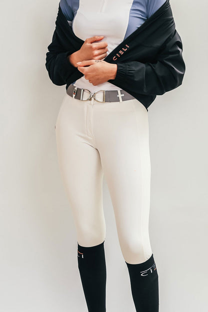 Person wearing white riding pants with a black jacket and black socks on a plain background