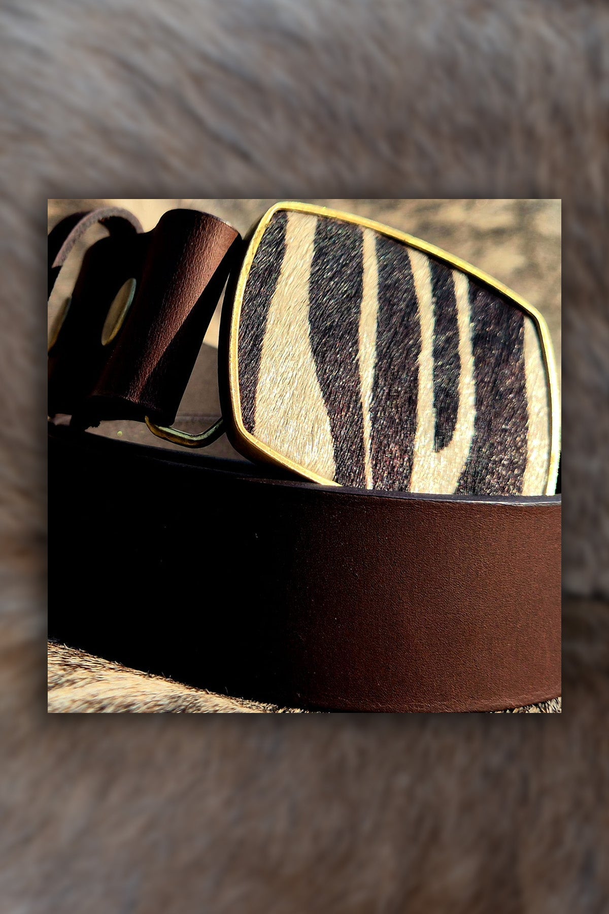 Brown leather belt with zebra pattern buckle on a fur background