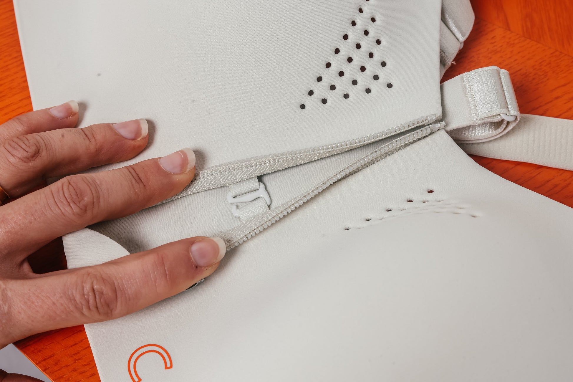 Hand zipping a white sports bra with an orange logo on a brown background