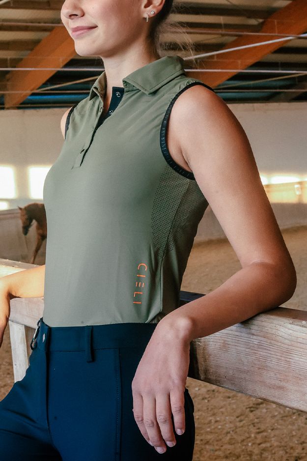 Woman wearing a green sleeveless shirt with a brand logo, standing in an indoor setting.