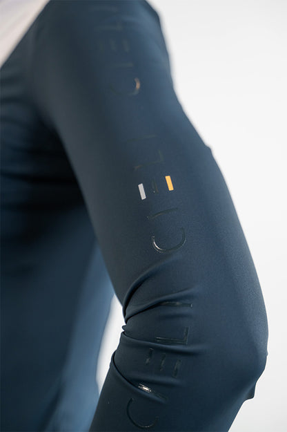 Close-up of a person's arm wearing dark navy athletic show shirt with embossed vertical lettering and a small white and orange logo near the upper forearm.